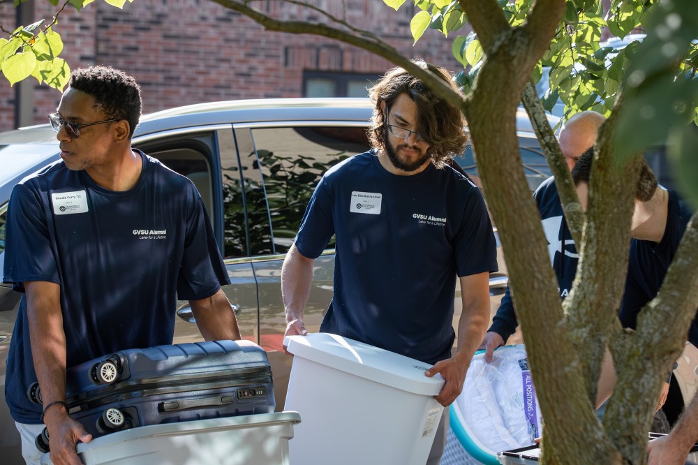 2 GVSU Alumni carrying gray boxes inside